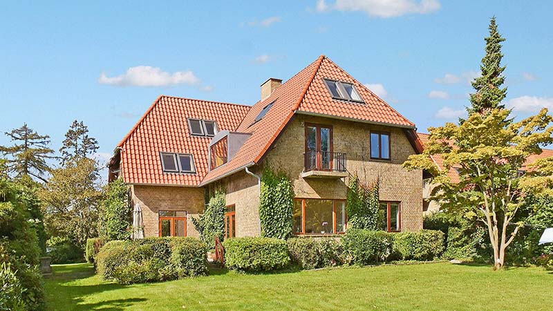 Rødt tegltag på gul murstensvilla med have